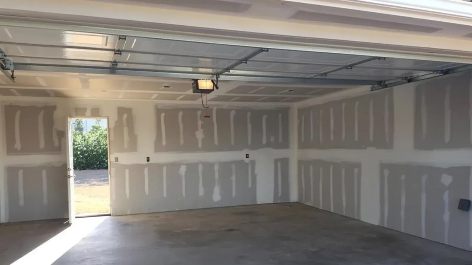 Attached garage with the walls and ceiling drywalled and taped, seen through the open overhead door